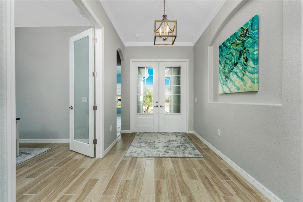 A bright entryway features light wood-look tile flooring, a glass-paneled double door, and wall art — 25223 KEYGRASS COURT, PUNTA GORDA, FL