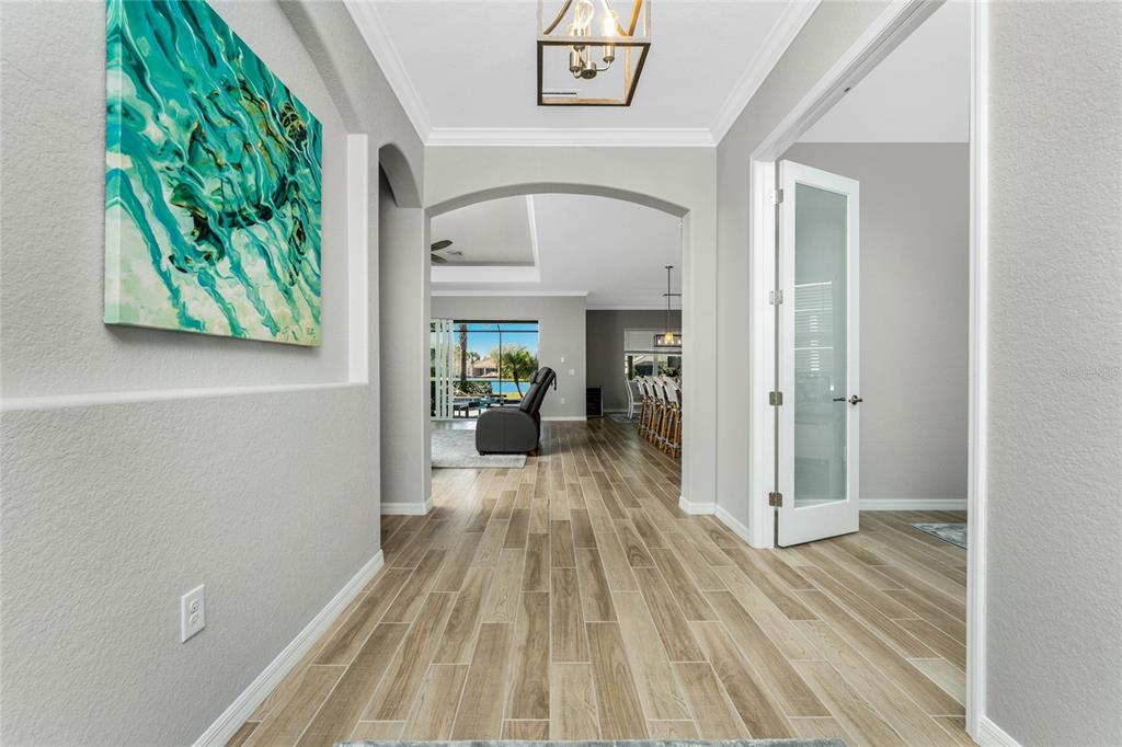A bright foyer with wood-look tile flooring leads through an arched doorway into a living area — 25223 KEYGRASS COURT, PUNTA GORDA, FL