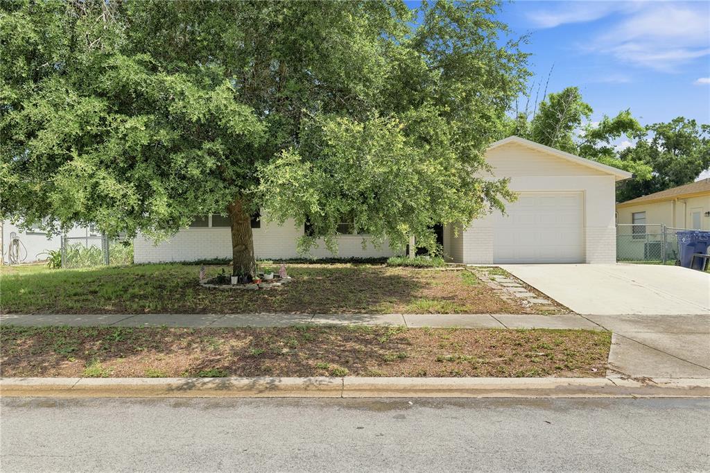 A single-story house with a white brick exterior, a front-facing garage, and a large tree — 7819 ROYAL STEWART DRIVE, NEW PORT RICHEY, FL