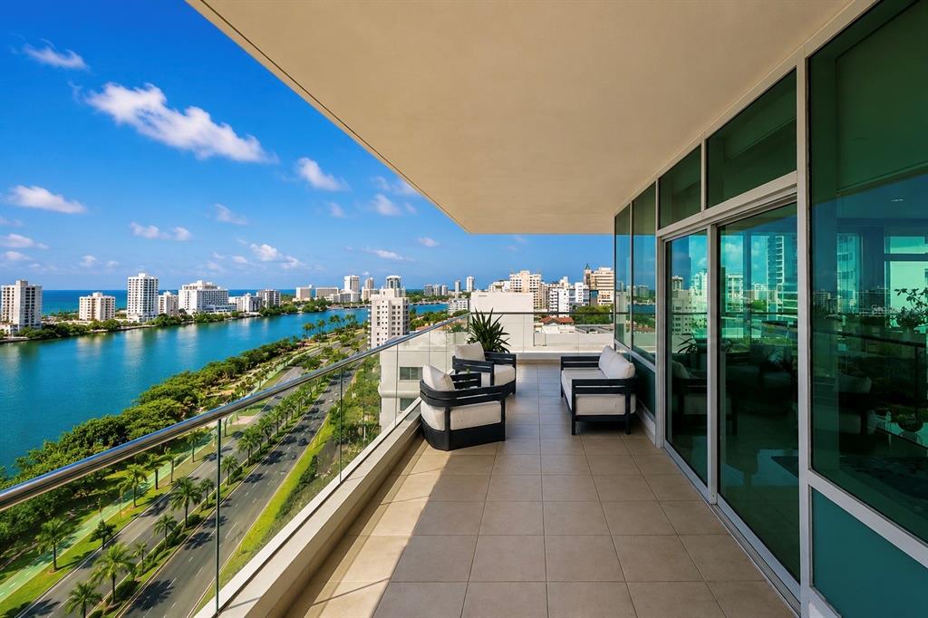 A balcony with outdoor seating overlooks a coastal city skyline, a waterway, and a road — 555 MONSERRATE, SAN JUAN, PR