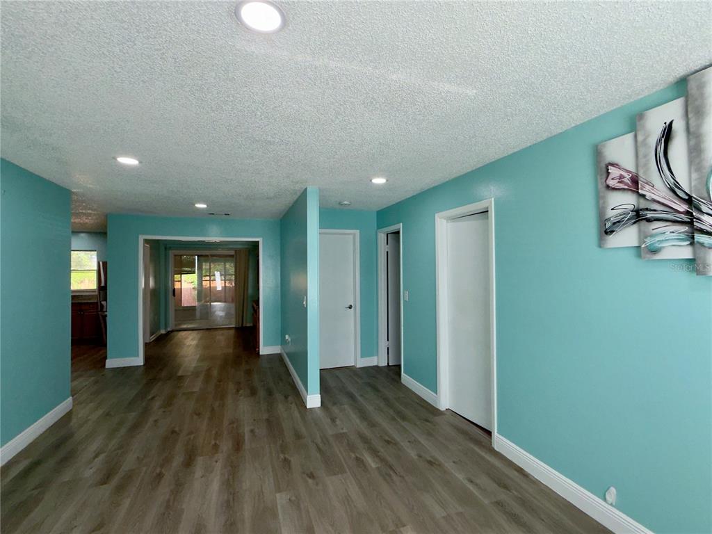 A room with turquoise walls, wood-look flooring, and recessed lighting leads toward a sliding glass door — 9805 LILY STREET N UNIT 9805, PINELLAS PARK, FL