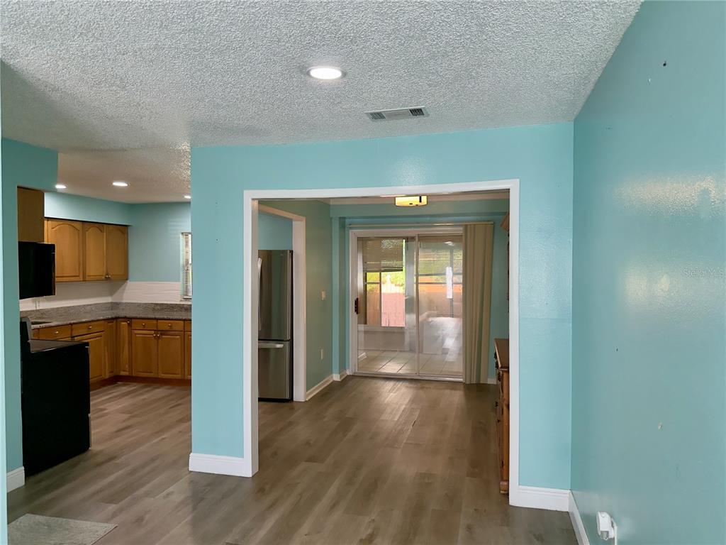 A kitchen with wood cabinets and light flooring opens into a dining area with sliding doors — 9805 LILY STREET N UNIT 9805, PINELLAS PARK, FL