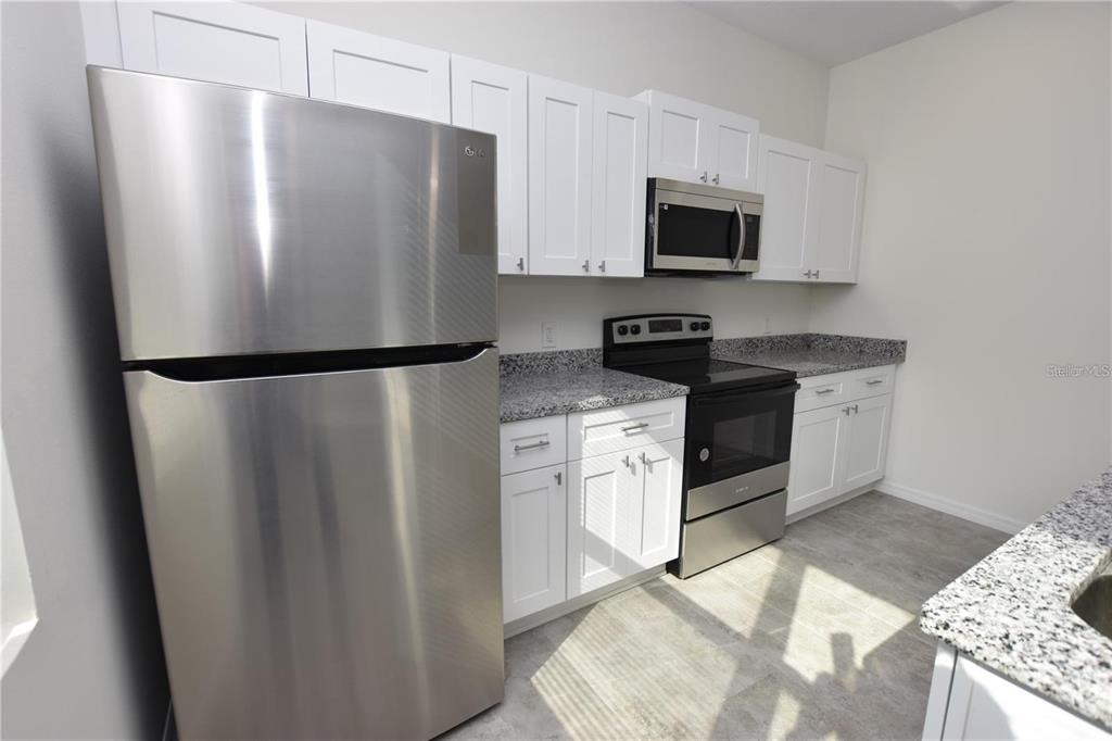 A kitchen features white cabinets, stainless steel appliances, and speckled granite countertops — 202 W CRESCENT DRIVE, LAKELAND, FL