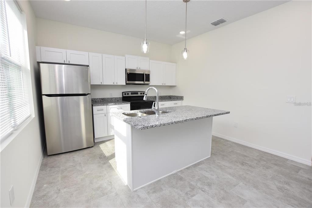 A kitchen featuring white cabinets, stainless steel appliances, a granite island, and gray tile flooring — 202 W CRESCENT DRIVE, LAKELAND, FL