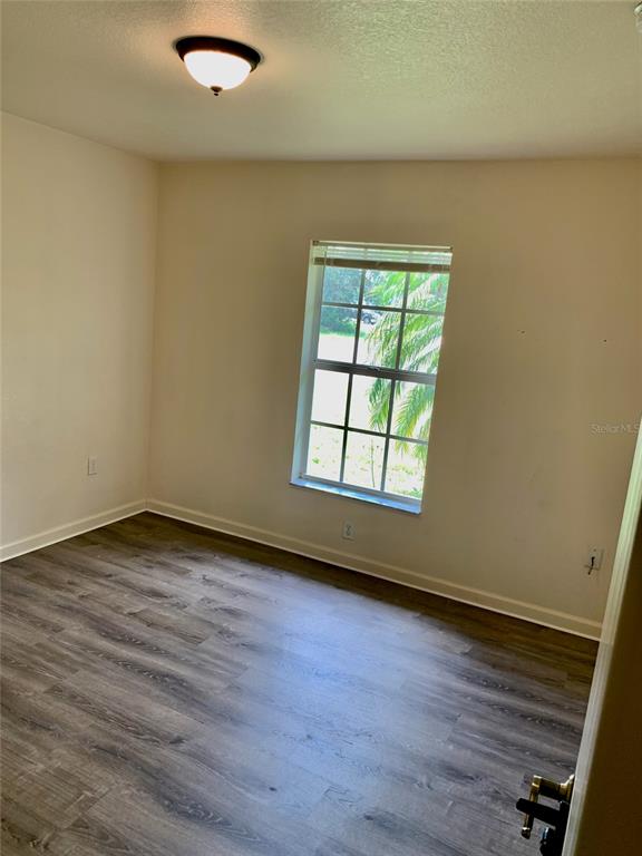 An empty bedroom features light-colored walls, a single window, and dark wood-look flooring — 8310 DELK AVENUE, NORTH PORT, FL