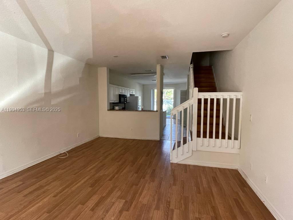 A living room features wood-look flooring, a staircase with a white railing, and an open kitchen — 3550 Oleander Ter, Riviera Beach FL 33404, RIVIERA BEACH, FL