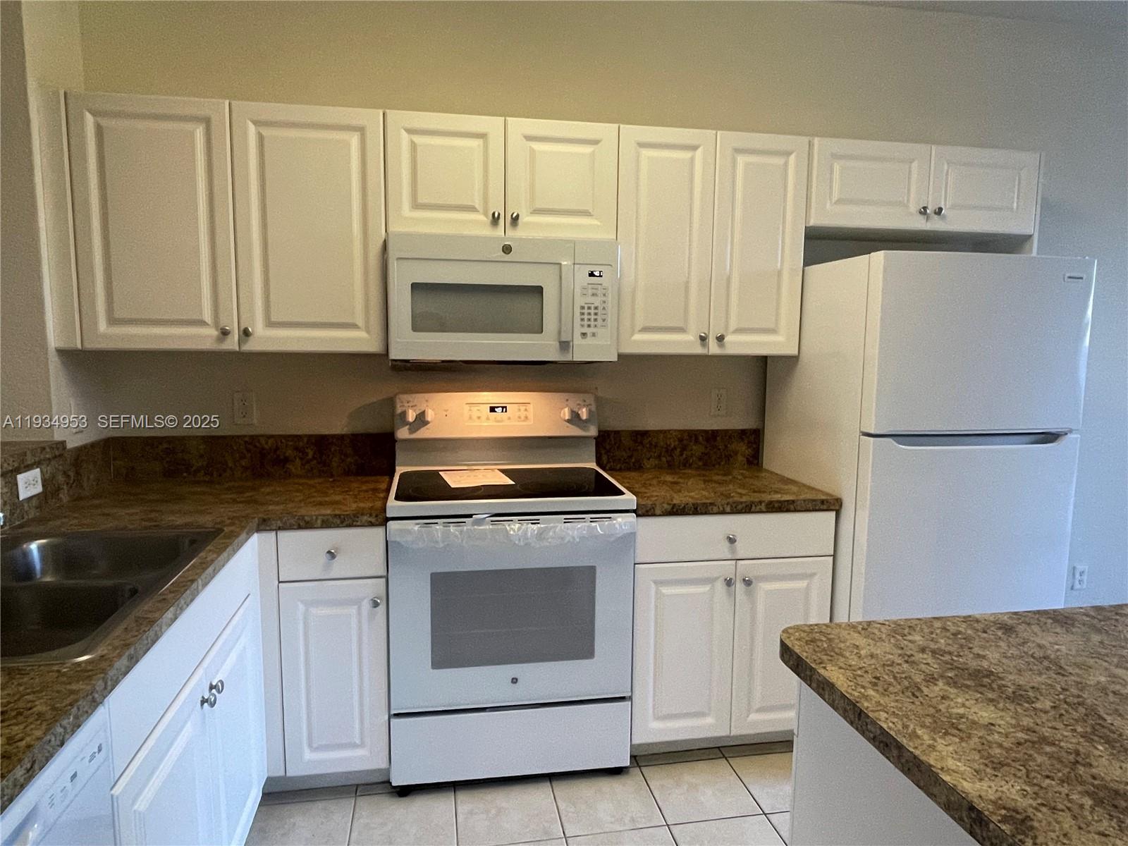 A kitchen features white cabinets, a white stove, a microwave, and brown countertops — 3550 Oleander Ter, Riviera Beach FL 33404, RIVIERA BEACH, FL