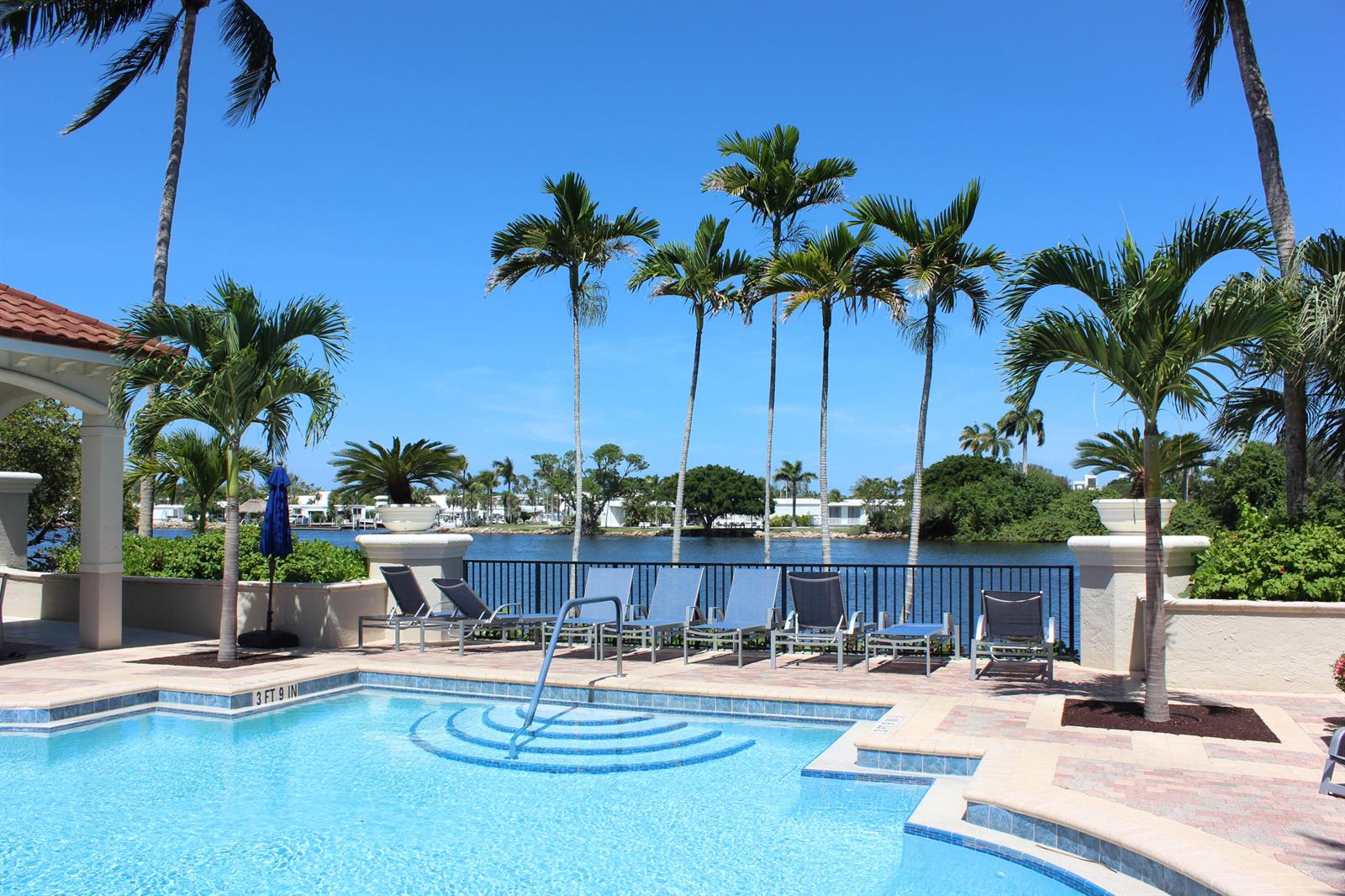 A swimming pool with lounge chairs and palm trees overlooks a canal on a sunny day — 3302 Tuscany Way, Boynton Beach FL 33435, BOYNTON BEACH, FL