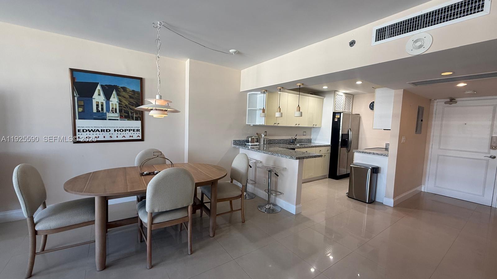 A dining area with a wooden table and chairs sits adjacent to a modern kitchen — 100 Lincoln Rd # 1108, Miami Beach FL 33139, MIAMI BEACH, FL