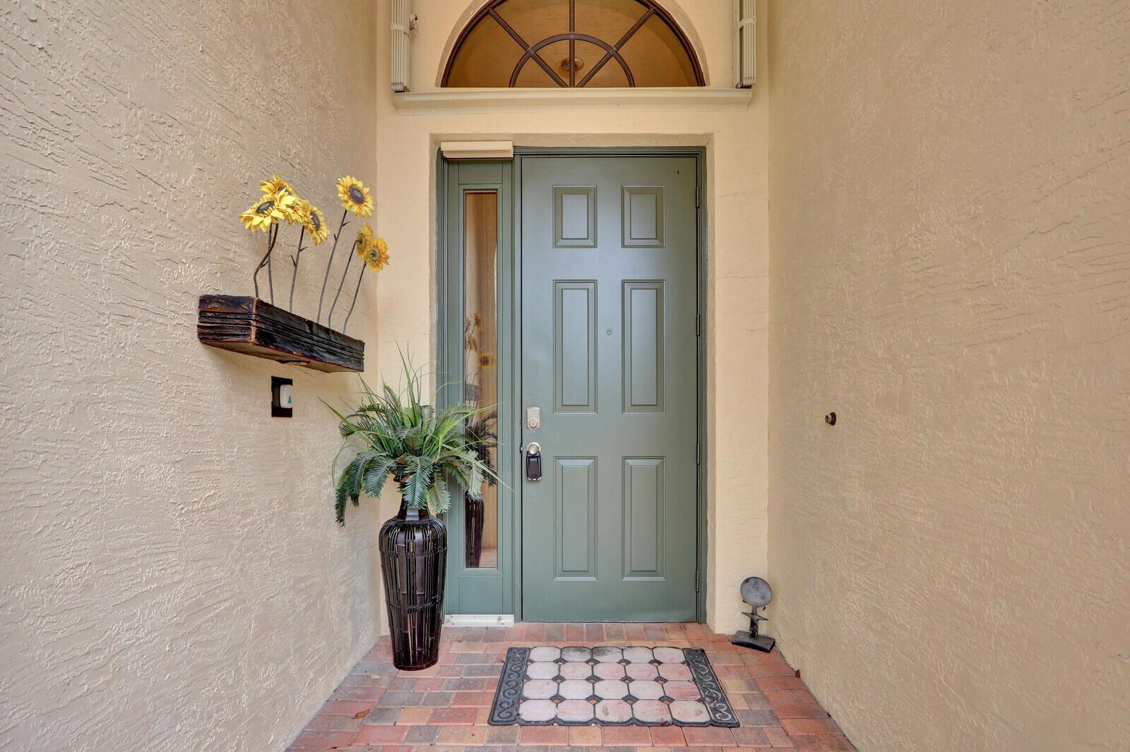 A green front door with a sidelight and arched transom window sits on a brick porch — 7159 Boscanni Drive, Boynton Beach FL 33437, BOYNTON BEACH, FL