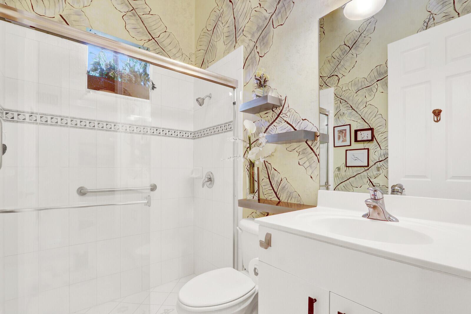 A bathroom with a glass-enclosed shower, white vanity, and walls featuring a large leaf pattern — 7159 Boscanni Drive, Boynton Beach FL 33437, BOYNTON BEACH, FL