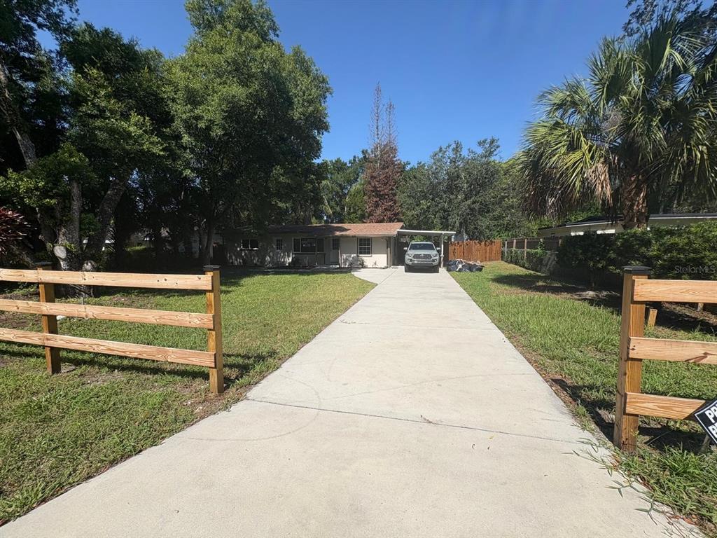 A single-story house with a long concrete driveway and a wooden fence in the foreground — 4358 BEDFORD ROAD, SANFORD, FL