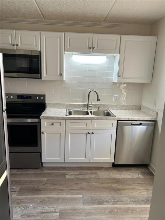 A kitchen features white cabinets, stainless steel appliances, a subway tile backsplash, and wood-look flooring — 4435 1ST STREET NE UNIT 111, ST PETERSBURG, FL