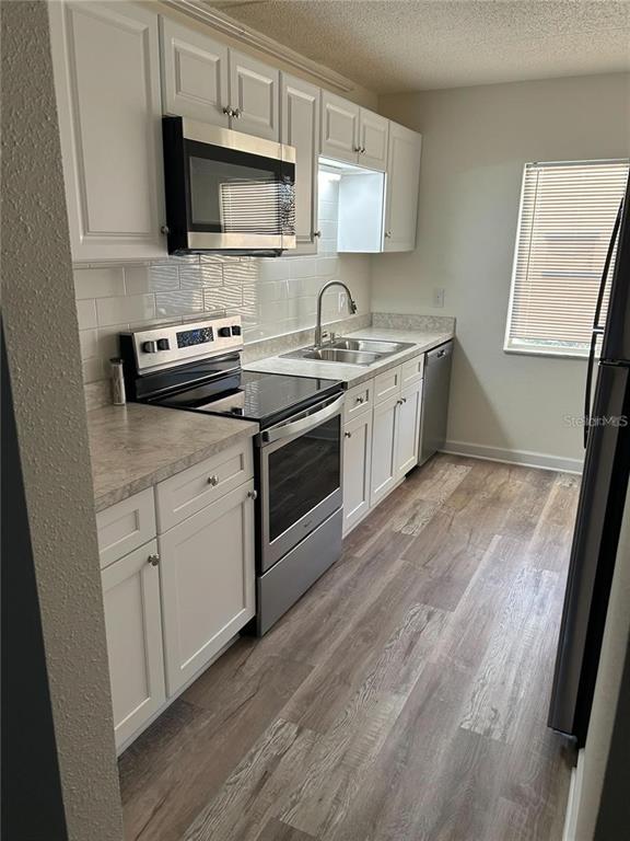 A galley-style kitchen features white cabinets, stainless steel appliances, and wood-look flooring — 4435 1ST STREET NE UNIT 111, ST PETERSBURG, FL
