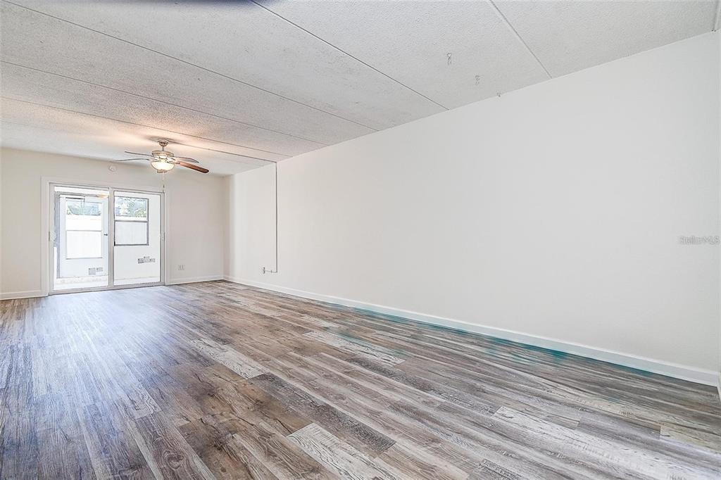 An empty room with wood-look flooring, a ceiling fan, and a sliding glass door — 4435 1ST STREET NE UNIT 111, ST PETERSBURG, FL