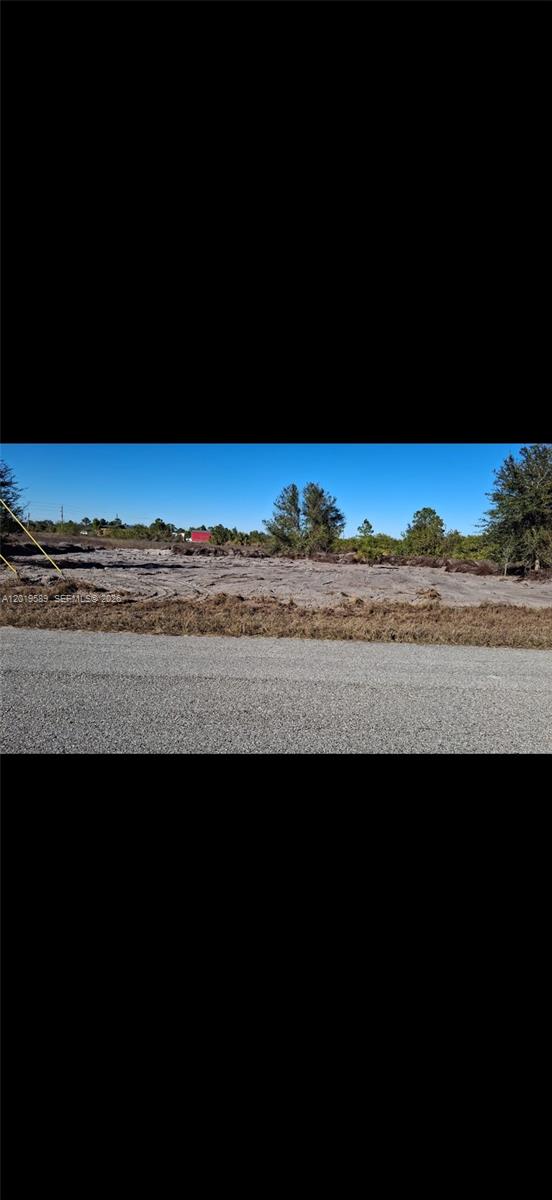 A cleared, sandy vacant lot sits adjacent to a paved road under a clear sky — 4005 E 15th St, Lehigh Acres FL 33972, LEHIGH ACRES, FL