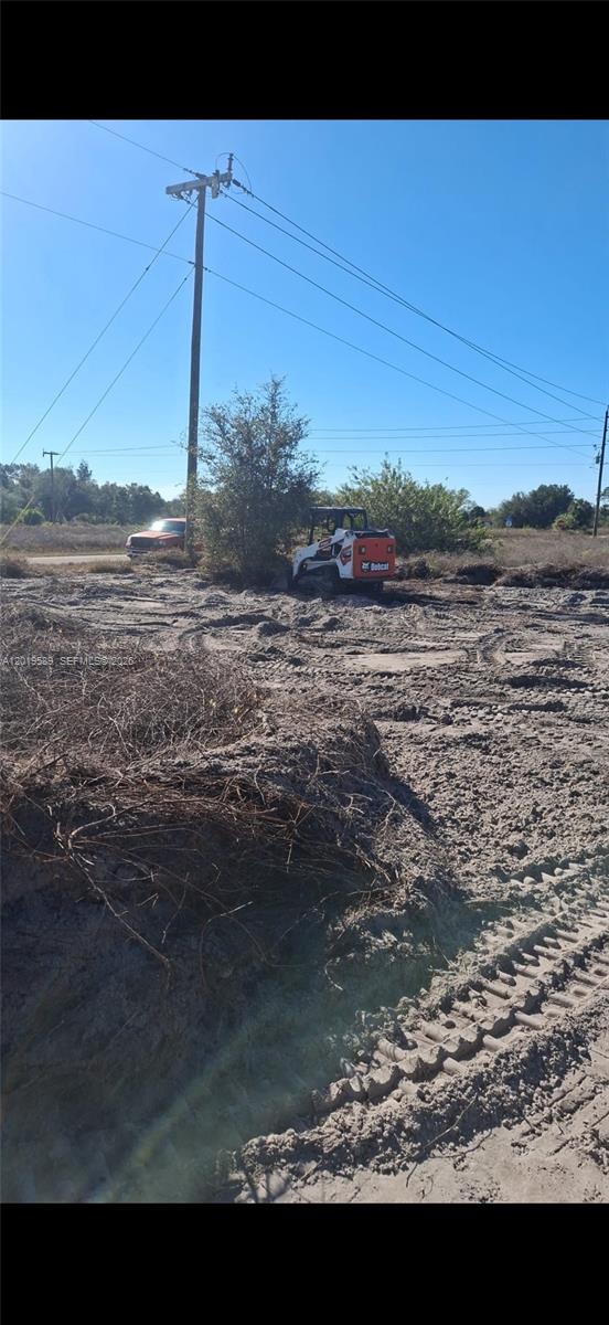 A skid steer loader works on a cleared, sandy lot with a utility pole nearby — 4005 E 15th St, Lehigh Acres FL 33972, LEHIGH ACRES, FL