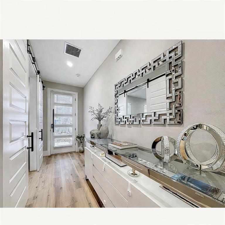 A modern entryway features a mirrored console table, a geometric wall mirror, and wood flooring — 2720 S SHINE AVENUE, ORLANDO, FL
