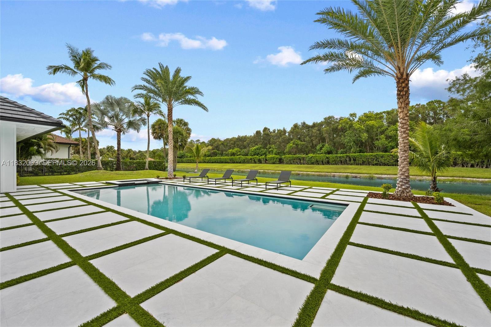 A rectangular swimming pool is surrounded by large pavers with grass inlays and palm trees — 1761 Breakers West Blvd, West Palm Beach FL 33411, WEST PALM BEACH, FL
