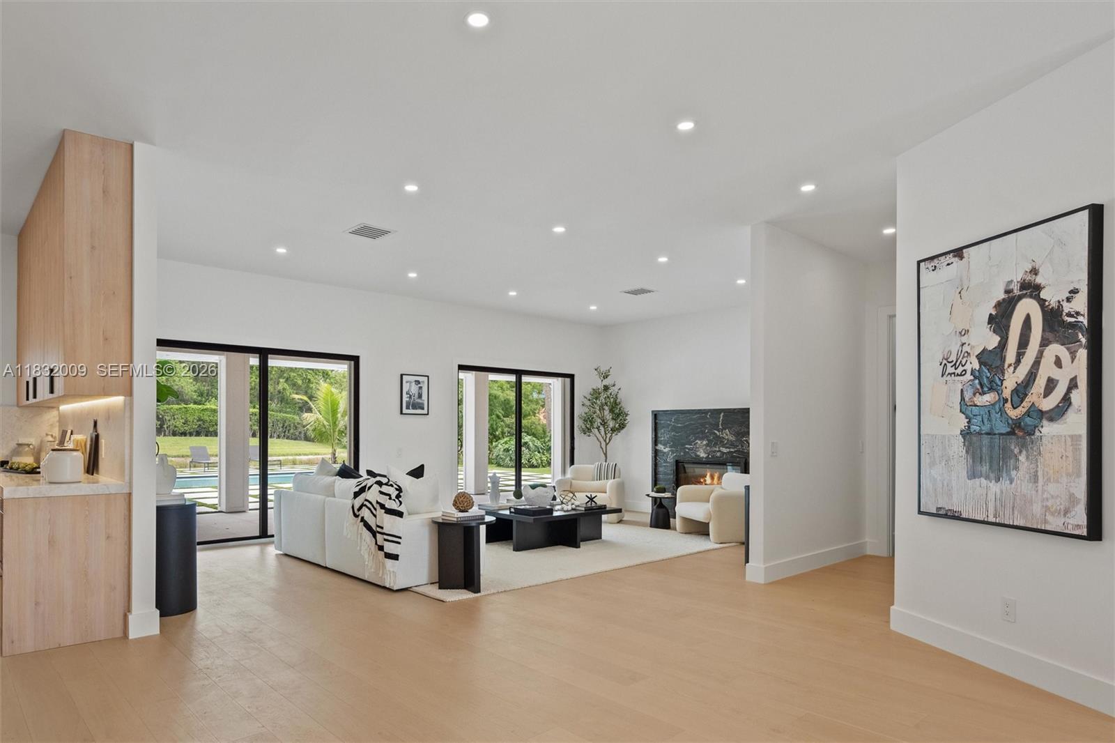 A modern living room features a marble fireplace, white sofas, and large sliding glass doors — 1761 Breakers West Blvd, West Palm Beach FL 33411, WEST PALM BEACH, FL
