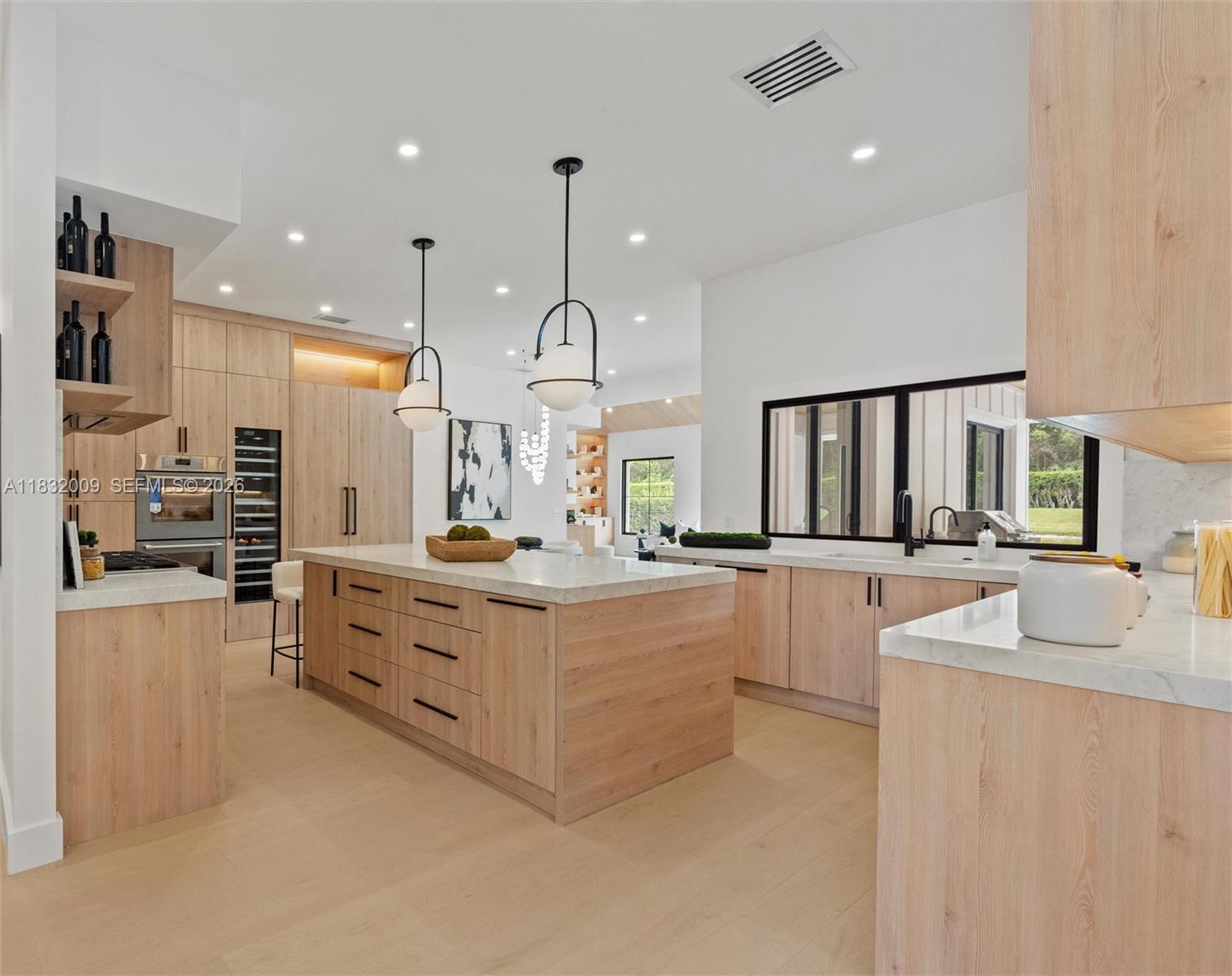 A modern kitchen features light wood cabinetry, a large central island, and white countertops — 1761 Breakers West Blvd, West Palm Beach FL 33411, WEST PALM BEACH, FL