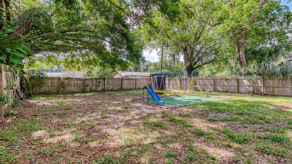 A backyard features a wooden fence, large shade trees, and a playground set with a slide — 2122 LAKE BOULEVARD, WINTER HAVEN, FL