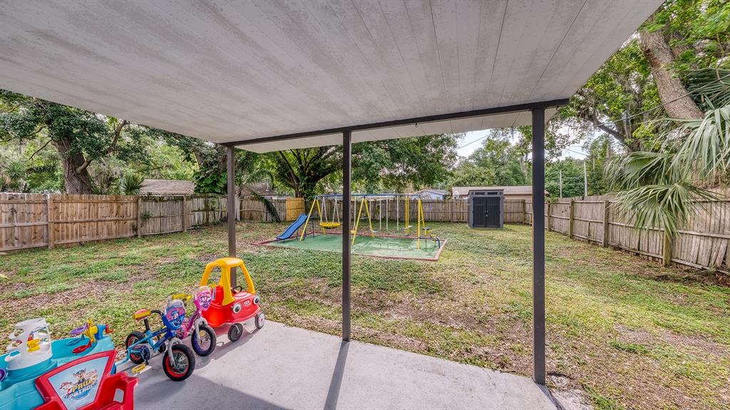 A covered concrete patio overlooks a fenced backyard with a swing set and children's toys — 2122 LAKE BOULEVARD, WINTER HAVEN, FL