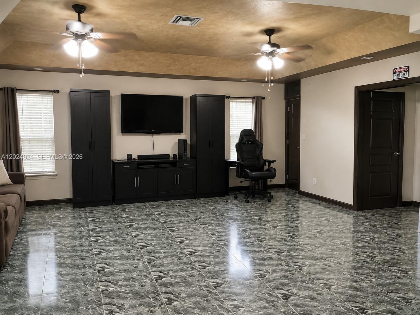 A living room features a tray ceiling, dark cabinetry, a wall-mounted television, and tiled flooring — 15530 SW 155th Ave, Miami FL 33187, MIAMI, FL