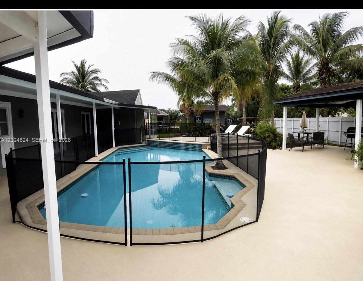 A backyard features a swimming pool enclosed by a black safety fence and a patio — 15530 SW 155th Ave, Miami FL 33187, MIAMI, FL