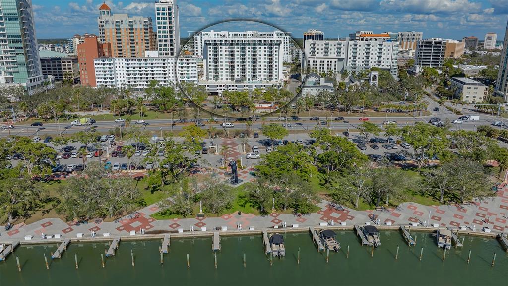 An aerial view of a white high-rise building located behind a waterfront park and marina — 101 S GULFSTREAM AVENUE UNIT 4J, SARASOTA, FL