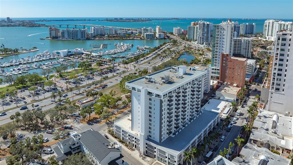 An aerial view shows a tall white apartment building near a marina and coastal city — 101 S GULFSTREAM AVENUE UNIT 4J, SARASOTA, FL