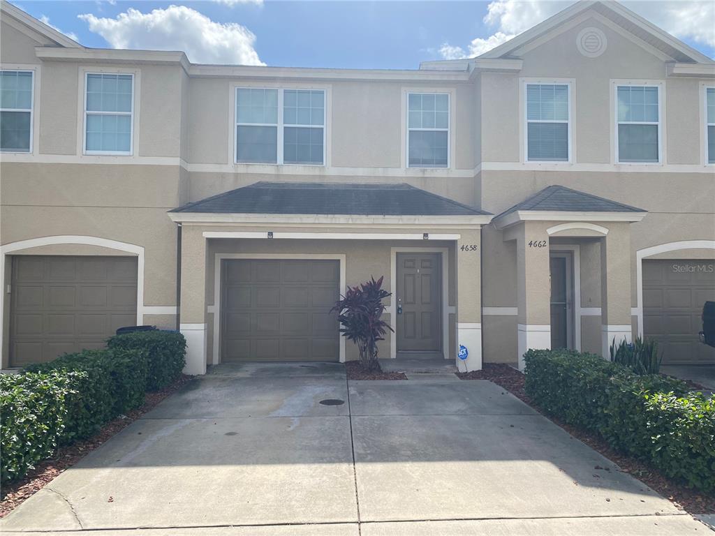 A two-story townhouse exterior features a beige stucco facade, a single-car garage, and a driveway — 4658 69TH PLACE NORTH, PINELLAS PARK, FL