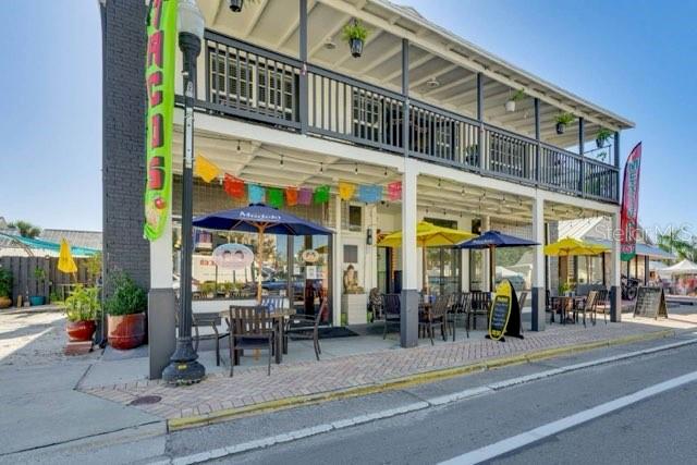 A two-story commercial building features a ground-level outdoor patio with tables and umbrellas — 209 W OLYMPIA AVENUE, PUNTA GORDA, FL