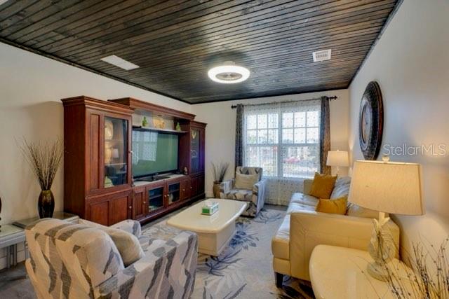 A living room features a dark wood-paneled ceiling, a large media console, and neutral furniture — 209 W OLYMPIA AVENUE, PUNTA GORDA, FL
