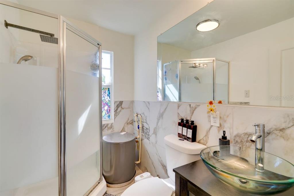 A bathroom features a glass vessel sink, marble-look tile walls, and a corner shower — 209 W OLYMPIA AVENUE, PUNTA GORDA, FL