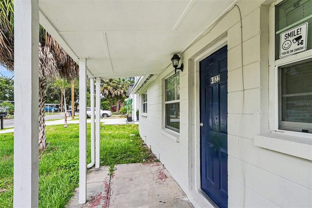 A white exterior wall with a blue front door and a covered concrete porch — 4022 E HENRY AVENUE, TAMPA, FL