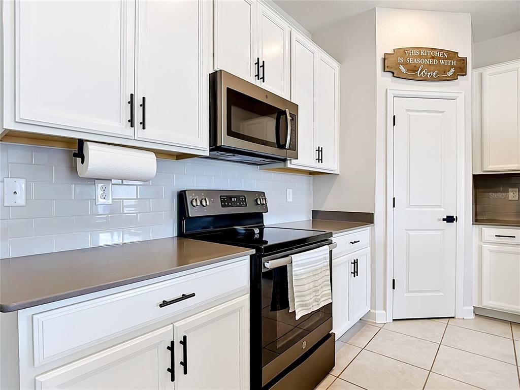 A kitchen features white cabinets, a stainless steel microwave, a black stove, and tile flooring — 237 TAFT DRIVE, DAVENPORT, FL