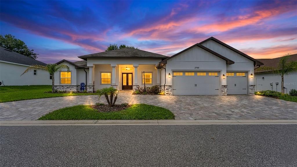 A single-story house with a paved driveway, three-car garage, and stone accents at sunset — 2729 SUNRISE LANDING LANE, LAKELAND, FL