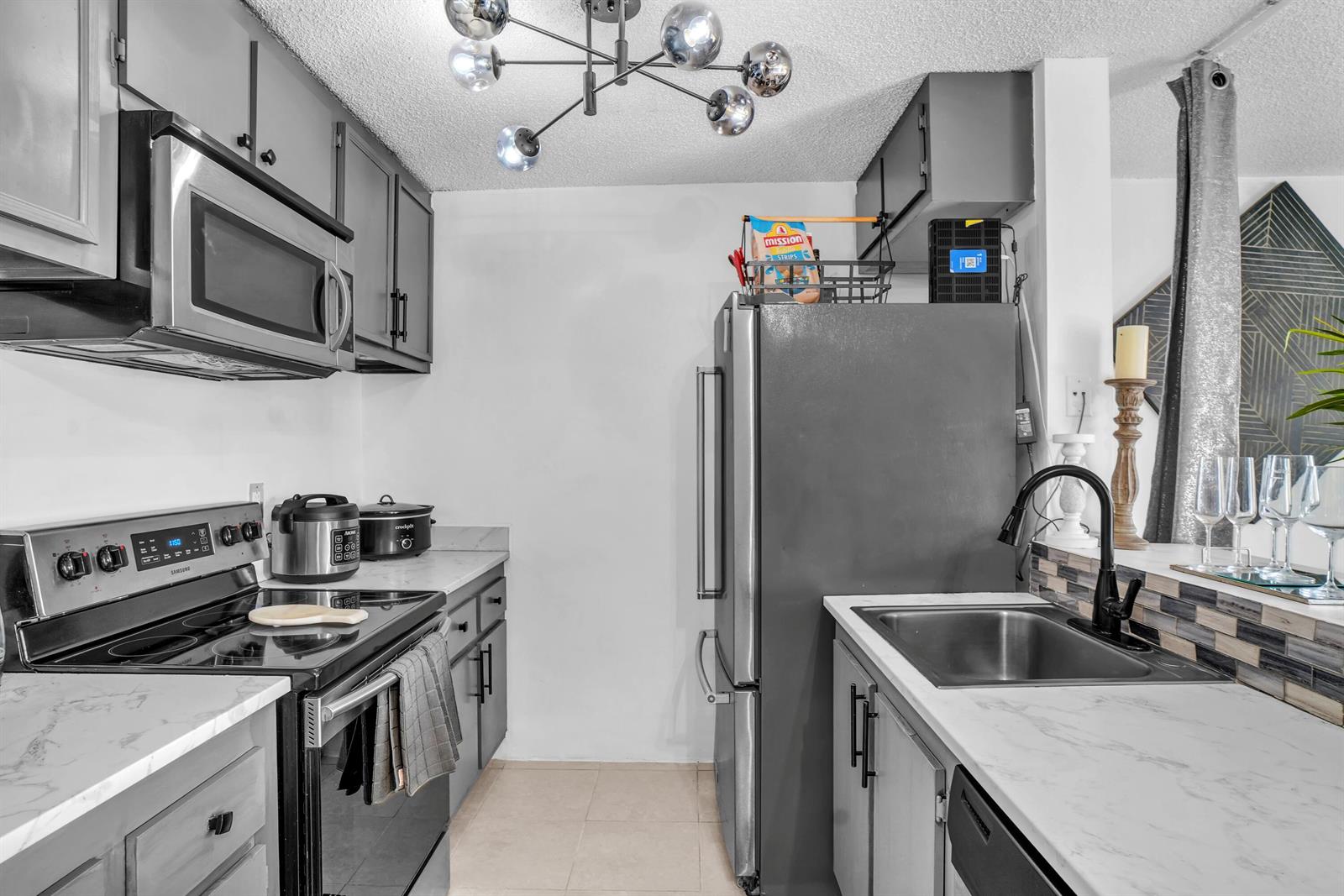 A kitchen features gray cabinets, stainless steel appliances, white marble-look countertops, and a modern chandelier — 1423 Meadows Circle W, Boynton Beach FL 33436, BOYNTON BEACH, FL