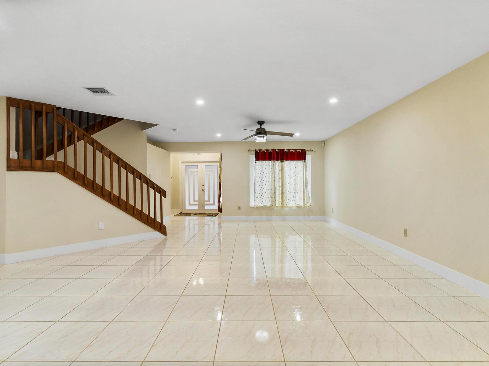 An empty room with beige tile flooring, a wooden staircase, and a ceiling fan — 22965 Old Inlet Bridge Drive, Boca Raton FL 33433, BOCA RATON, FL