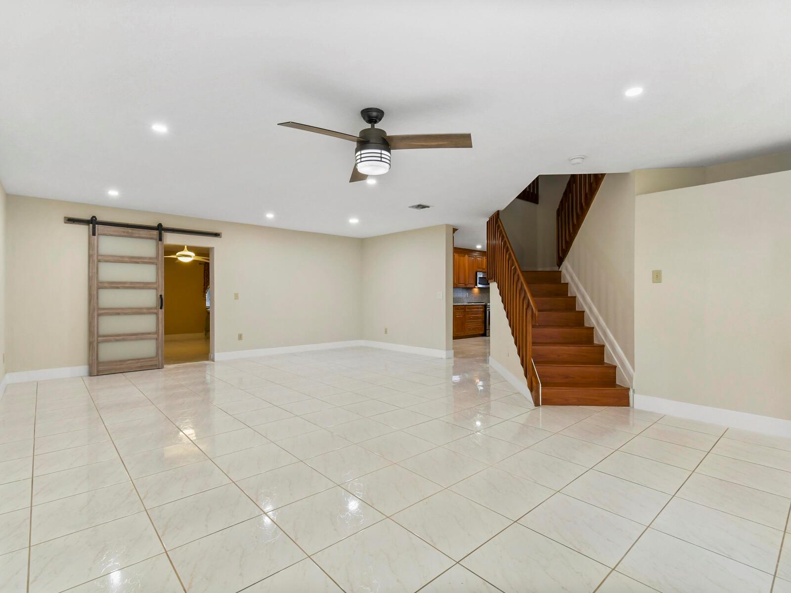 A spacious room with white tile flooring, a ceiling fan, a barn door, and wooden stairs — 22965 Old Inlet Bridge Drive, Boca Raton FL 33433, BOCA RATON, FL