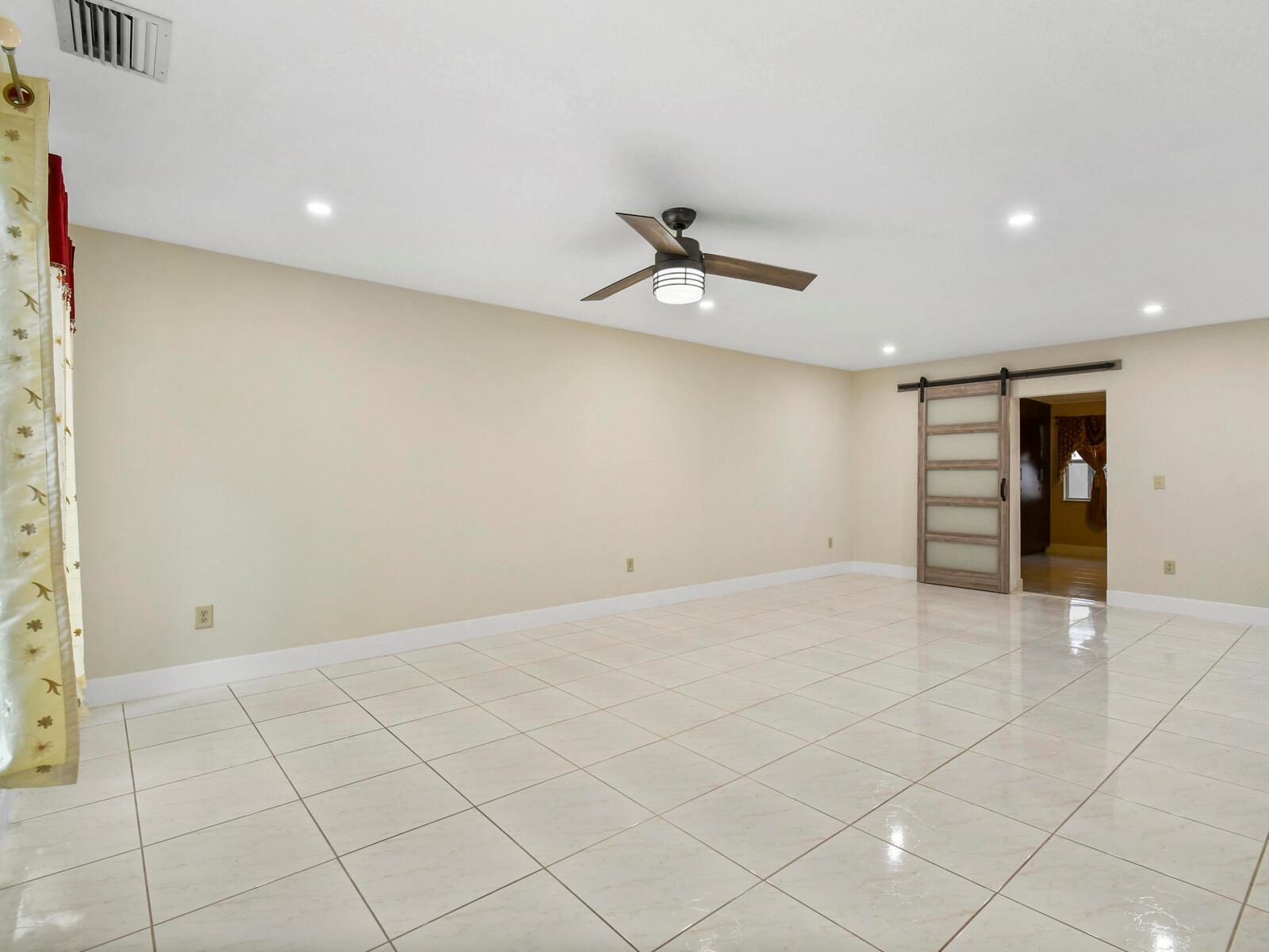 A spacious room with light-colored tile flooring, a ceiling fan, and a sliding barn door — 22965 Old Inlet Bridge Drive, Boca Raton FL 33433, BOCA RATON, FL