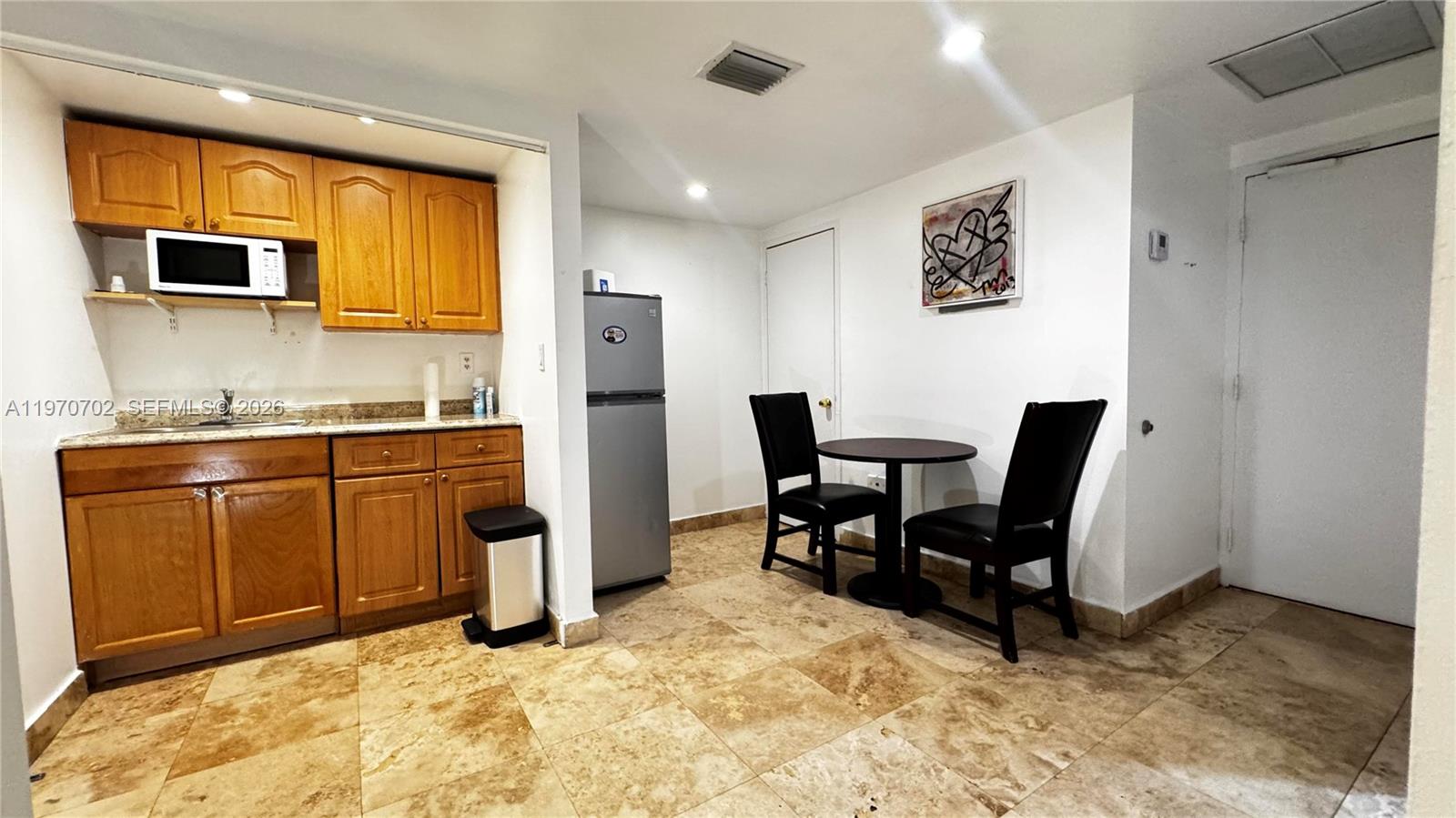 A kitchen area features wooden cabinets, a small dining table with two chairs, and tile flooring — 999 Brickell Bay Dr # 303, Miami FL 33131, MIAMI, FL