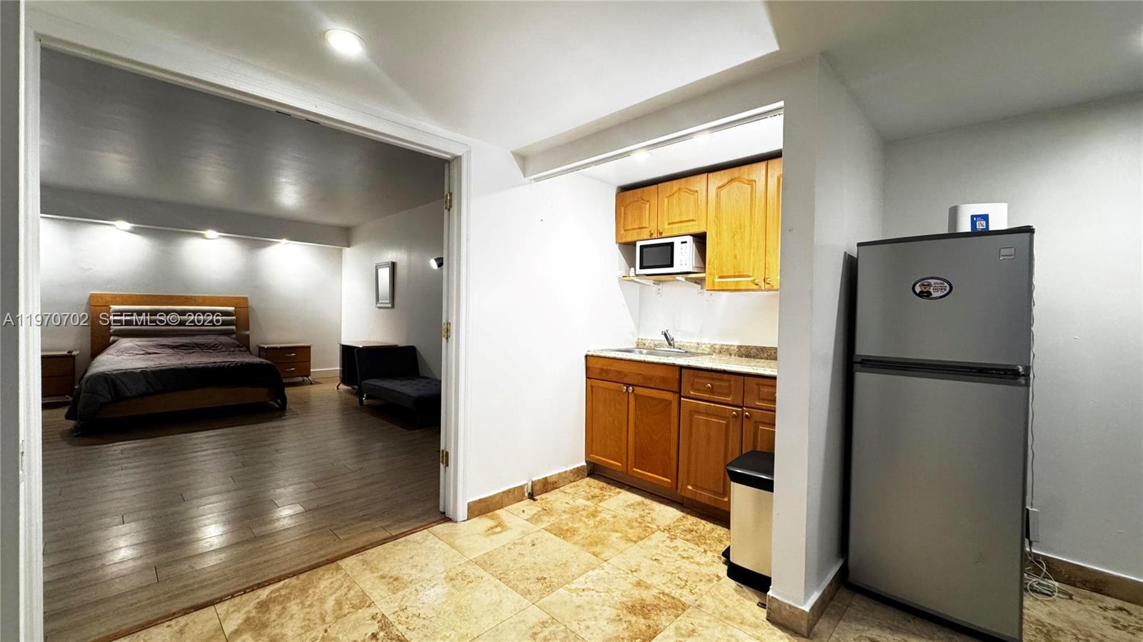 A small kitchenette with wooden cabinets sits adjacent to a bedroom with wood flooring — 999 Brickell Bay Dr # 303, Miami FL 33131, MIAMI, FL