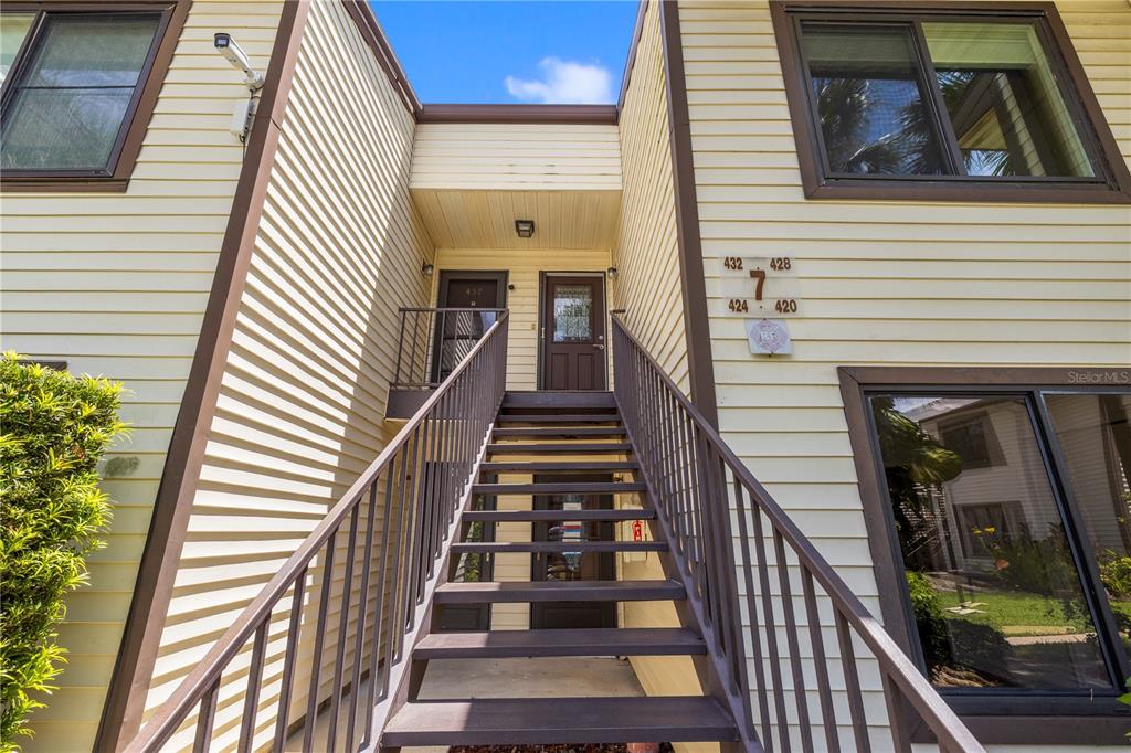 An exterior view of a two-story apartment building with stairs leading to upper-level units — 428 MOORINGS COVE DRIVE UNIT 7F, TARPON SPRINGS, FL