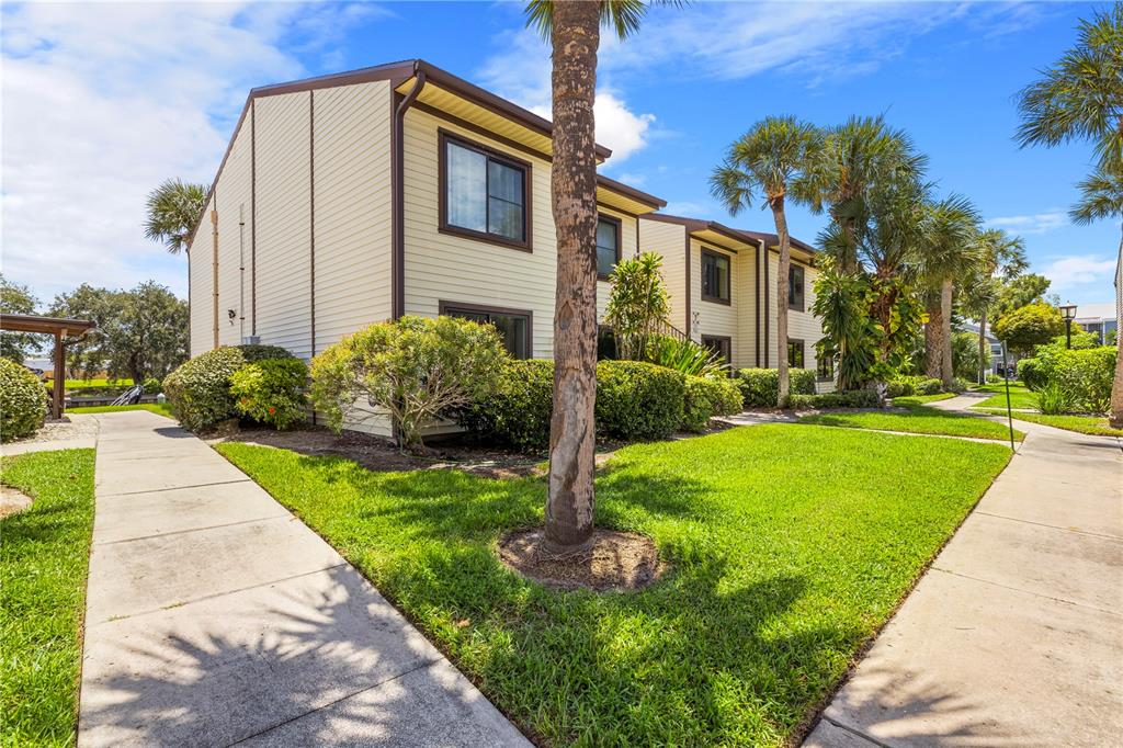 A two-story apartment building with beige siding stands beside a sidewalk and green lawn — 428 MOORINGS COVE DRIVE UNIT 7F, TARPON SPRINGS, FL