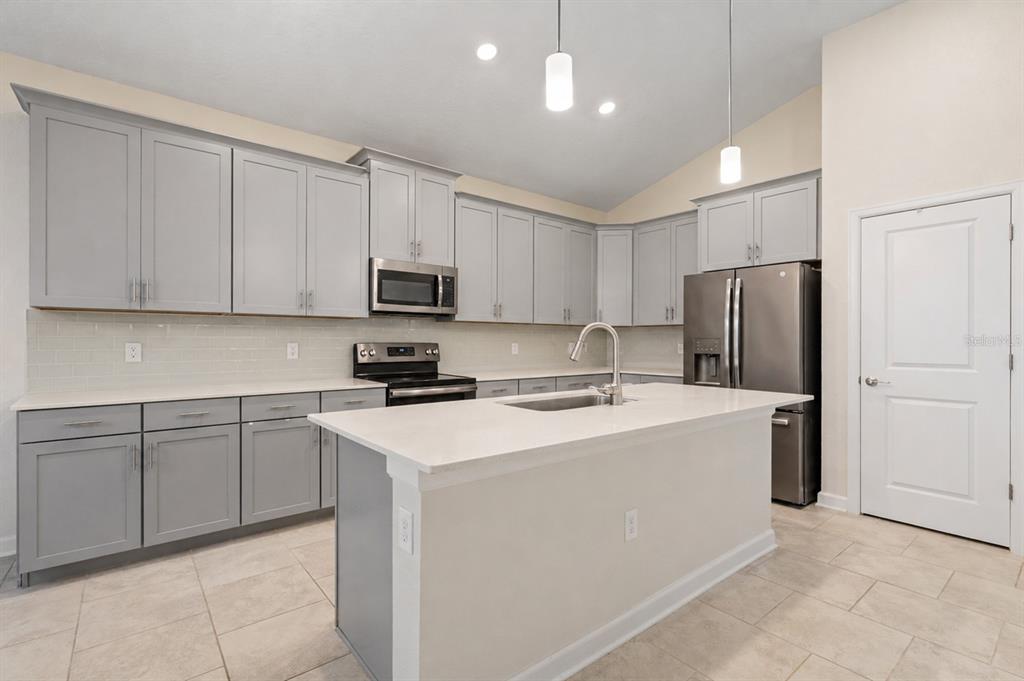 A kitchen features gray cabinets, white countertops, stainless steel appliances, and a central island — 1478 OLYMPIC CLUB BOULEVARD, CHAMPIONS GATE, FL