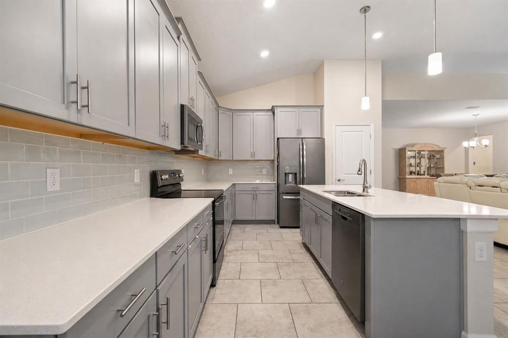 A modern kitchen features gray cabinets, white countertops, a subway tile backsplash, and stainless appliances — 1478 OLYMPIC CLUB BOULEVARD, CHAMPIONS GATE, FL