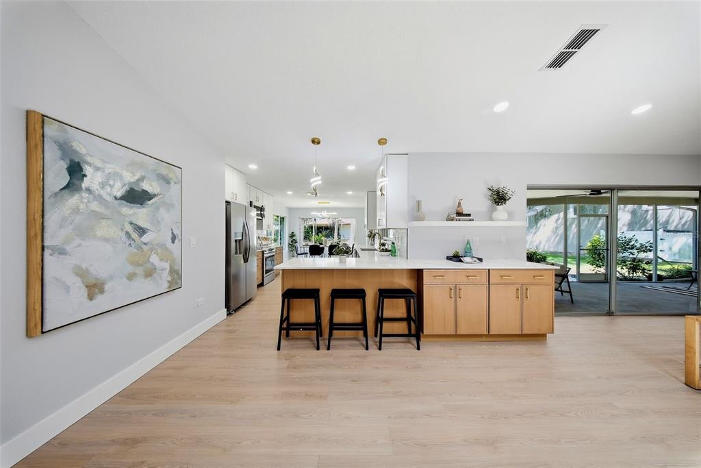 A modern kitchen features light wood cabinets, a white island with barstools, and sliding doors — 4301 MARINE PARKWAY, NEW PORT RICHEY, FL