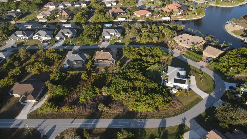 An aerial view shows a vacant, wooded residential lot surrounded by houses and a canal — 9399 PANAMA CIRCLE, PORT CHARLOTTE, FL